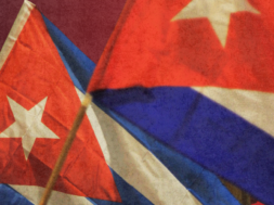 A imagem mostra duas bandeiras de Cuba tremulando em destaque, com seus icônicos tons de vermelho, branco e azul.