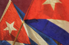 A imagem mostra duas bandeiras de Cuba tremulando em destaque, com seus icônicos tons de vermelho, branco e azul.