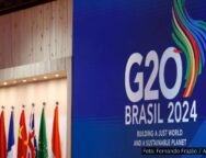 Painel azul com o logotipo do G20 Brasil 2024, acompanhado de bandeiras de países membros e a frase "Building a Just World and a Sustainable Planet".