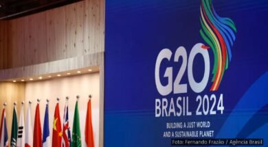 Painel azul com o logotipo do G20 Brasil 2024, acompanhado de bandeiras de países membros e a frase "Building a Just World and a Sustainable Planet".