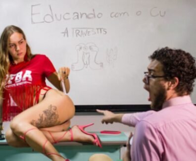 Imagem de uma performance artística, onde Tertuliana Lustosa, com camiseta vermelha, posa em cima de uma mesa de frente para um quadro branco, com um espectador expressando surpresa. No quadro, está escrito "Educando com o C* - A Travestis".