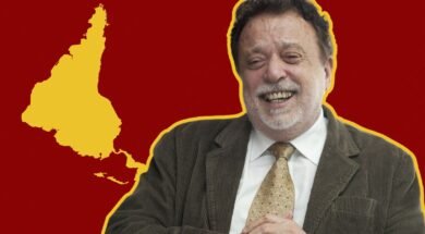 Fotografia de Theotônio dos Santos sorrindo, vestindo terno e gravata, com um mapa da América Latina invertido em relação à cartografia eurocêntrica. O mapa está em amarelo sobre um fundo vermelho listrado.