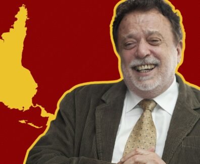 Fotografia de Theotônio dos Santos sorrindo, vestindo terno e gravata, com um mapa da América Latina invertido em relação à cartografia eurocêntrica. O mapa está em amarelo sobre um fundo vermelho listrado.