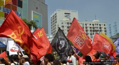 Manifestantes em ato político segurando bandeiras de movimentos sociais e organizações, como PCB e UJC, em frente a prédios urbanos. Foto: Rafa Torres / @f0tografah