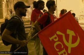 Grupo de jovens militantes da UJC no Piauí em ato público, com uma bandeira vermelha do PCB em destaque, em ambiente ao ar livre.
