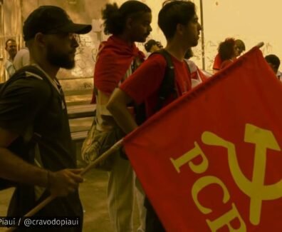 Grupo de jovens militantes da UJC no Piauí em ato público, com uma bandeira vermelha do PCB em destaque, em ambiente ao ar livre.