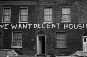 Fachada da Ocupaçao Connolly Barrack, na Irlanda, com uma faixa escrito "WE WANT DECENT HOUSING!"