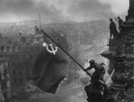 Foto preto e branco que retrata soldado soviético balançando bandeira da URSS na Berlim conquistada, no dia 9 de maio, marcando o dia que ficaria conhecido como Dia da Vitória