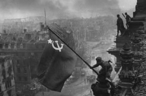Foto preto e branco que retrata soldado soviético balançando bandeira da URSS na Berlim conquistada, no dia 9 de maio, marcando o dia que ficaria conhecido como Dia da Vitória