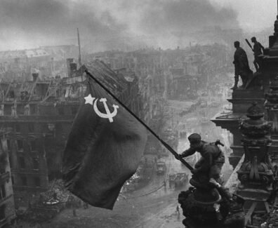 Foto preto e branco que retrata soldado soviético balançando bandeira da URSS na Berlim conquistada, no dia 9 de maio, marcando o dia que ficaria conhecido como Dia da Vitória