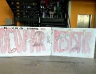 Um quadro branco colocado à frente de uma escada, limitando toda a sua extensão. Nele, está escrito, em vermelho e preto: "Paralização estudantil já! Ocupar e Resistir!". Atrás do quadro, no primeiro lance de escadas, várias cadeiras estão jogadas, sobrepostas umas às outras.