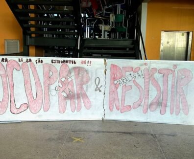 Um quadro branco colocado à frente de uma escada, limitando toda a sua extensão. Nele, está escrito, em vermelho e preto: "Paralização estudantil já! Ocupar e Resistir!". Atrás do quadro, no primeiro lance de escadas, várias cadeiras estão jogadas, sobrepostas umas às outras.