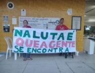 Duas pessoas seguram uma faixa escrita 'Na luta é que a gente se encontra' em frente a uma parede com azulejos amarelos, dentro de uma universidade. Uma delas veste camisa da MUP (Movimento por uma Universidade Popular). Foto: Reprodução / MUP - São Mateus.
