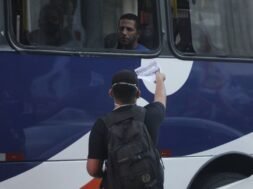 Jovem entregando um panfleto pela janela de um ônibus para um homem.