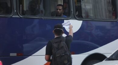 Jovem entregando um panfleto pela janela de um ônibus para um homem.