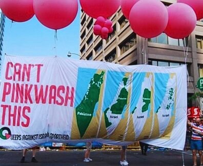 Foto de manifestação com balões rosas e uma grande faixa escrito "Não tem como fazer pinkwash disso", do movimento Queers contra o Apartheid Israelense.
