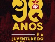 Imagem quadrada com fundo em tons escuros de vermelho e preto com textura pontilhada. Ao centro da imagem, em letras grandes amarelas, está escrito "98". O número "9" está à esquerda e o "8" à direita. Dentro do número "8", no topo, há o símbolo da UJC: uma estrela vermelha com foice e martelo amarelos, e abaixo dela um retângulo vermelho com as letras brancas "UJC". Abaixo dos números, centralizado, está escrito em letras amarelas: "ANOS". Mais abaixo, também centralizado, aparece a frase "É A JUVENTUDE DO PCB", em que "É A" e "JUVENTUDE DO" estão em letras amarelas e "PCB" está em letras amarelas acompanhadas do símbolo da foice e martelo à esquerda da sigla. Acima e abaixo da frase há linhas horizontais brancas.