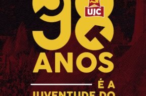 Imagem quadrada com fundo em tons escuros de vermelho e preto com textura pontilhada. Ao centro da imagem, em letras grandes amarelas, está escrito "98". O número "9" está à esquerda e o "8" à direita. Dentro do número "8", no topo, há o símbolo da UJC: uma estrela vermelha com foice e martelo amarelos, e abaixo dela um retângulo vermelho com as letras brancas "UJC". Abaixo dos números, centralizado, está escrito em letras amarelas: "ANOS". Mais abaixo, também centralizado, aparece a frase "É A JUVENTUDE DO PCB", em que "É A" e "JUVENTUDE DO" estão em letras amarelas e "PCB" está em letras amarelas acompanhadas do símbolo da foice e martelo à esquerda da sigla. Acima e abaixo da frase há linhas horizontais brancas.