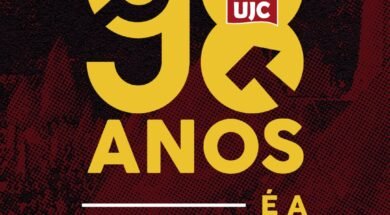 Imagem quadrada com fundo em tons escuros de vermelho e preto com textura pontilhada. Ao centro da imagem, em letras grandes amarelas, está escrito "98". O número "9" está à esquerda e o "8" à direita. Dentro do número "8", no topo, há o símbolo da UJC: uma estrela vermelha com foice e martelo amarelos, e abaixo dela um retângulo vermelho com as letras brancas "UJC". Abaixo dos números, centralizado, está escrito em letras amarelas: "ANOS". Mais abaixo, também centralizado, aparece a frase "É A JUVENTUDE DO PCB", em que "É A" e "JUVENTUDE DO" estão em letras amarelas e "PCB" está em letras amarelas acompanhadas do símbolo da foice e martelo à esquerda da sigla. Acima e abaixo da frase há linhas horizontais brancas.