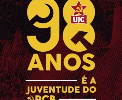 Imagem quadrada com fundo em tons escuros de vermelho e preto com textura pontilhada. Ao centro da imagem, em letras grandes amarelas, está escrito "98". O número "9" está à esquerda e o "8" à direita. Dentro do número "8", no topo, há o símbolo da UJC: uma estrela vermelha com foice e martelo amarelos, e abaixo dela um retângulo vermelho com as letras brancas "UJC". Abaixo dos números, centralizado, está escrito em letras amarelas: "ANOS". Mais abaixo, também centralizado, aparece a frase "É A JUVENTUDE DO PCB", em que "É A" e "JUVENTUDE DO" estão em letras amarelas e "PCB" está em letras amarelas acompanhadas do símbolo da foice e martelo à esquerda da sigla. Acima e abaixo da frase há linhas horizontais brancas.