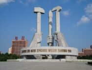 Na imagem tem três mãos em estátua, uma segurando um martelo simbolizando os trabalhadores da cidade, na esquerda, atrás segurando um pincel representando os intelectuais, e na direita a foice, representando os trabalhadores do campo.