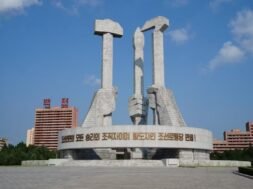 Na imagem tem três mãos em estátua, uma segurando um martelo simbolizando os trabalhadores da cidade, na esquerda, atrás segurando um pincel representando os intelectuais, e na direita a foice, representando os trabalhadores do campo.