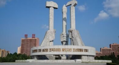 Na imagem tem três mãos em estátua, uma segurando um martelo simbolizando os trabalhadores da cidade, na esquerda, atrás segurando um pincel representando os intelectuais, e na direita a foice, representando os trabalhadores do campo.