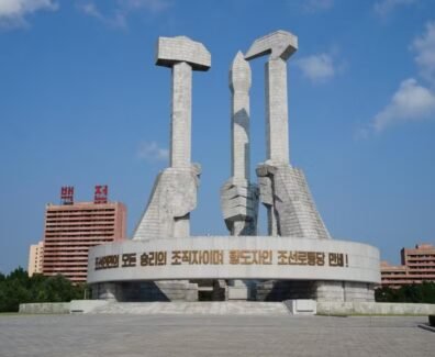 Na imagem tem três mãos em estátua, uma segurando um martelo simbolizando os trabalhadores da cidade, na esquerda, atrás segurando um pincel representando os intelectuais, e na direita a foice, representando os trabalhadores do campo.