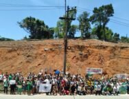 Moradores reunidos à frente de um morro completamente desmatado, segurando faixas, cartazes e bandeiras. Foto: UJC Brasil / Núcleo DC-SJM.