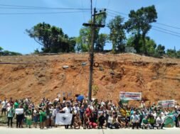Moradores reunidos à frente de um morro completamente desmatado, segurando faixas, cartazes e bandeiras. Foto: UJC Brasil / Núcleo DC-SJM.