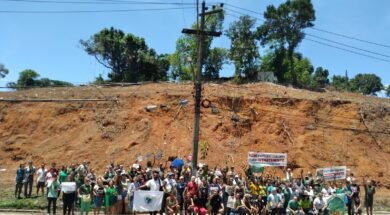 Moradores reunidos à frente de um morro completamente desmatado, segurando faixas, cartazes e bandeiras. Foto: UJC Brasil / Núcleo DC-SJM.