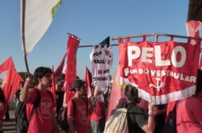 Grupo de estudantes em manifestação ao ar livre, vestindo camisetas vermelhas e segurando bandeiras e faixas; uma delas diz “Pelo fim do vestibular”, enquanto outras defendem pautas como Universidade Popular e melhores condições de estudo. Foto: Amanda Braun / UJC Brasil.