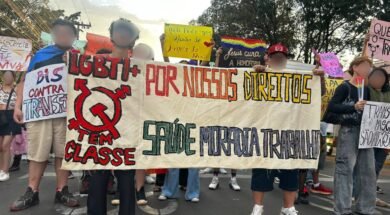 Registro fotográfico de militantes da população LGBTI+ com uma faixa branca escrito “LGBTI+ Tem classe, Por nossos direitos, saúde, moradia e trabalho” Outres ao fundo seguram cartazes que trazem mensagens de apoio à população LGBT e críticas à LGBTfobia. Foto: Lucas Nogueira / UJC Brasil.