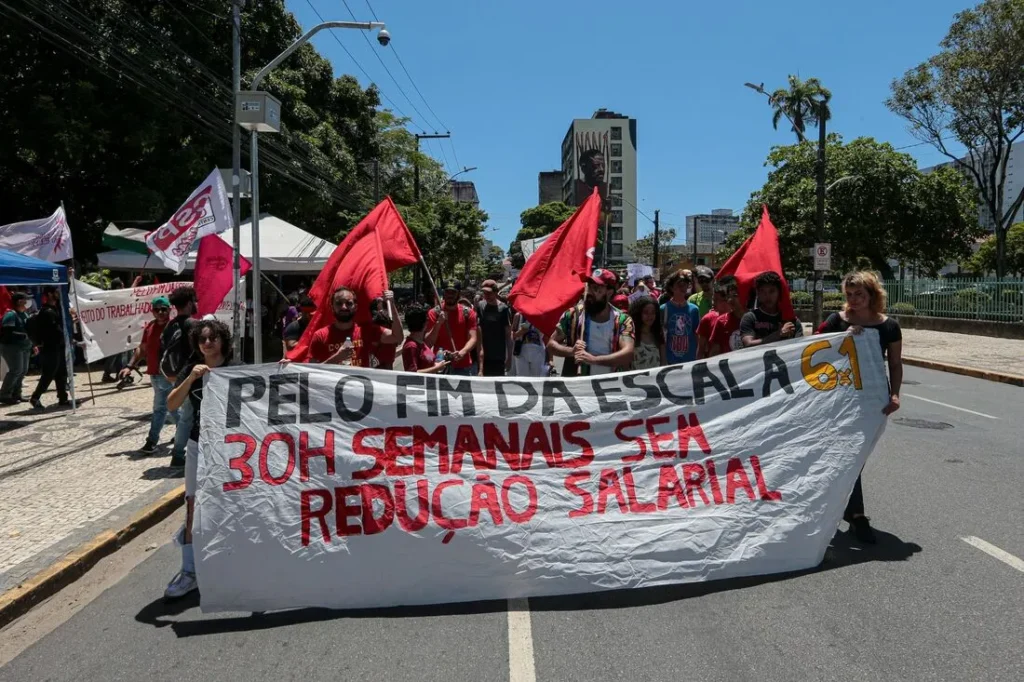 Faixa "PELO FIM DA ESCALA 6X1, 30H SEMANAIS SEM REDUÇÃO SALARIAL" exibida em ato de rua contra a escala 6x1. Foto Rafael Melo / Folha de Pernambuco.