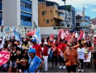 Pessoas andando no farol da Barra, segurando bandeiras de sindicatos vermelhas, brancas e amarelas, manifestando o desejo de acabar com uma escala 6x1.