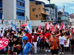 Pessoas andando no farol da Barra, segurando bandeiras de sindicatos vermelhas, brancas e amarelas, manifestando o desejo de acabar com uma escala 6x1.