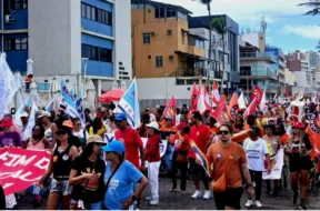 Pessoas andando no farol da Barra, segurando bandeiras de sindicatos vermelhas, brancas e amarelas, manifestando o desejo de acabar com uma escala 6x1.