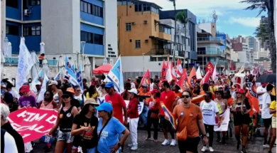 Pessoas andando no farol da Barra, segurando bandeiras de sindicatos vermelhas, brancas e amarelas, manifestando o desejo de acabar com uma escala 6x1.