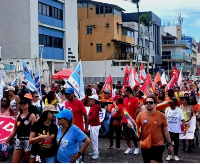 Pessoas andando no farol da Barra, segurando bandeiras de sindicatos vermelhas, brancas e amarelas, manifestando o desejo de acabar com uma escala 6x1.